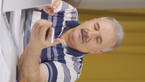 Vertical-video-of-Home-office-worker-old-man-getting-good-news-on-the-phone.